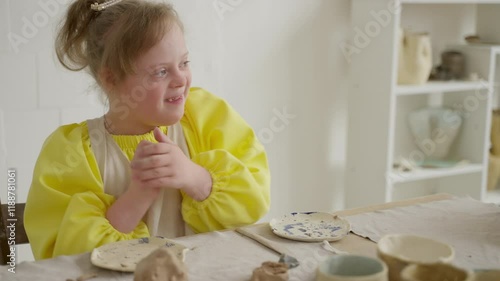 Child with Down syndrome joyfully chats with instructor while making pottery in inclusive workshop. Scene promotes social inclusion through activities. Concept: social acceptance, inclusive education photo