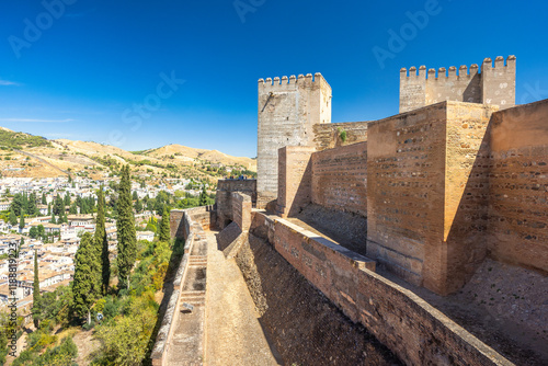 The Alcazaba fortress at the Alhambra complex in Granada town, Andalusia, Spain. Ancient fortress walls overlooking a city nestled in hills.  A sunny day reveals the aged stone and distant cityscape.