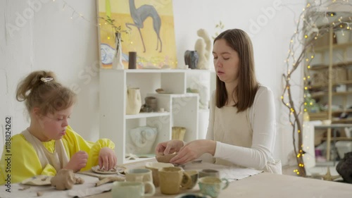 Child with Down syndrome and female instructor craft together in bright pottery studio, highlighting social inclusion. Scene underscores importance of acceptance and belonging in educational settings photo