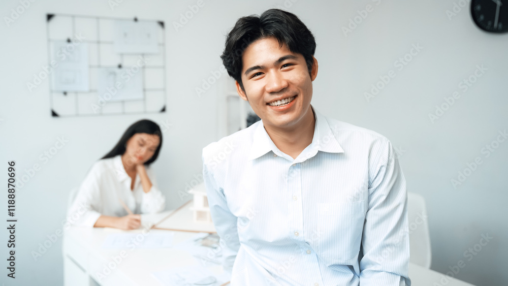 Professional happy businessman smiles during looking at camera. Young beautiful caucasian colleague drawing a blueprint on meeting table with house model and blueprint at modern office. Immaculate. Professional happy businessman smiles during looking at camera. Young beautiful caucasian colleague drawing a blueprint on meeting table with house model and blueprint at modern office. Immaculate.