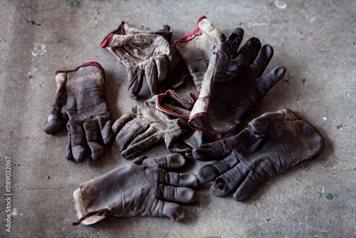 Several used dirty work gloves lying on concrete floor with blurred background.