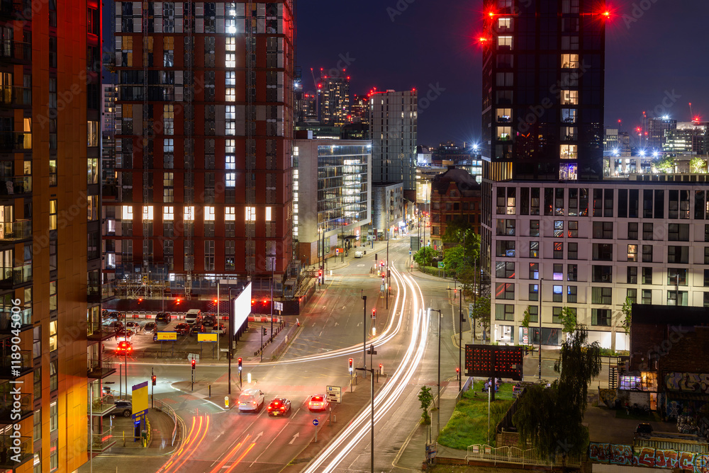 Elevated view of a busy crossroads lined with modern residential towers and shops in a urban setting at night. Manchester, UK. Elevated view of a busy crossroads lined with modern residential towers and shops in a urban setting at night. Manchester, UK.