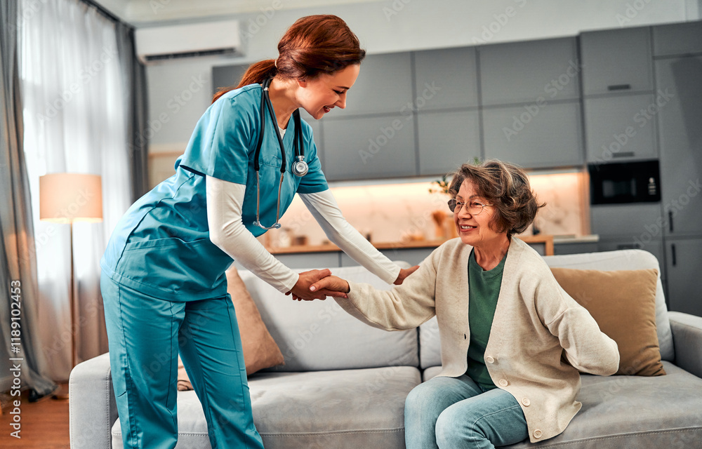 Obraz premium Geriatric doctor at home or in rehabilitation center. Nurse in blue uniform helps elderly patient to get up from sofa. Caregiver takes care of woman. Care, health care and assistance.