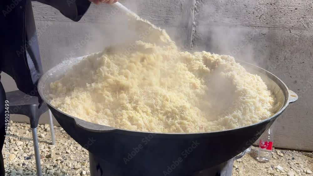 Fragment: An unidentified man stirs rice in a large cauldron. Cooking pilaf outdoors at a fair. Fragment: An unidentified man stirs rice in a large cauldron. Cooking pilaf outdoors at a fair.