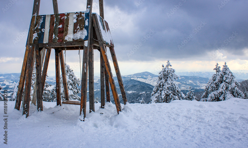 A snowy mountain scene on Divčibare with a swing overlooking a breathtaking viewpoint. The serene landscape is blanketed in snow, offering a peaceful winter atmosphere. A snowy mountain scene on Divčibare with a swing overlooking a breathtaking viewpoint. The serene landscape is blanketed in snow, offering a peaceful winter atmosphere.