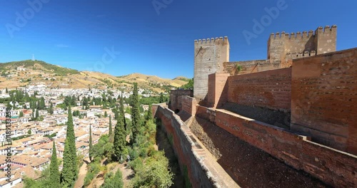 The Alcazaba fortress at the Alhambra complex in Granada town, Andalusia, Spain. Ancient fortress walls overlooking a city nestled in a valley under a clear blue sky.