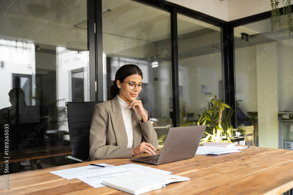 Fototapeta premium Young professional it specialist latin hispanic business lady working on laptop pc sitting at desk in modern office space. 30s middle eastern indian woman using computer technology app for work online