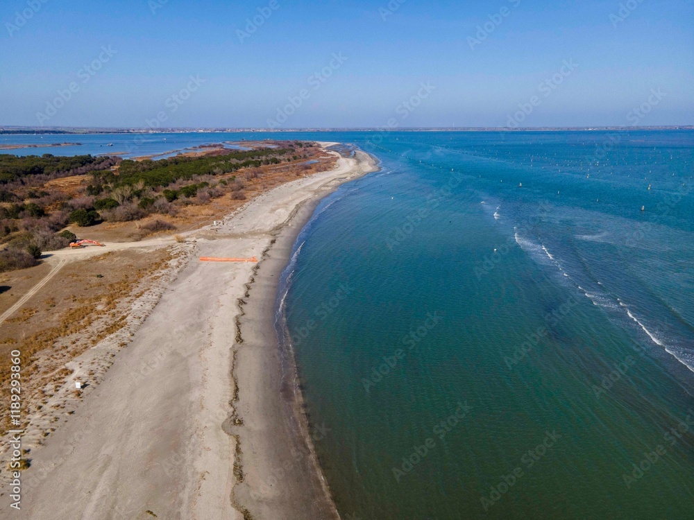 Aerial view of Lido di Volano's pristine shoreline meeting the calm blue waters of the Adriatic Sea. The sandy beach stretches along a tranquil, unspoiled coastal landscape. Aerial view of Lido di Volano's pristine shoreline meeting the calm blue waters of the Adriatic Sea. The sandy beach stretches along a tranquil, unspoiled coastal landscape.