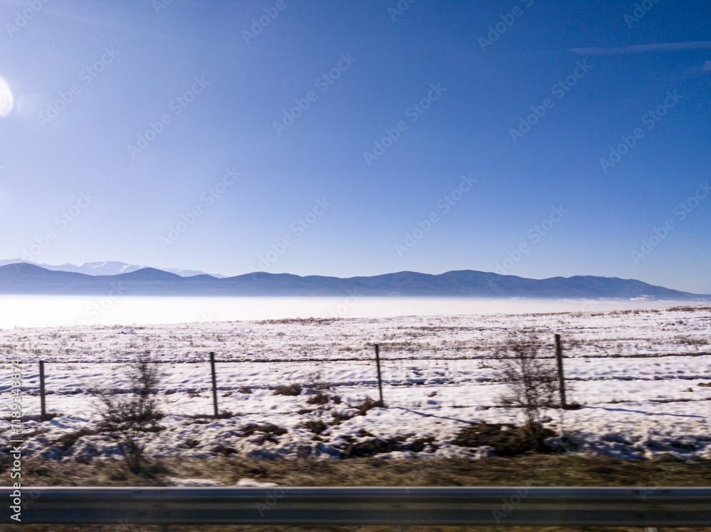 View to field and mountain with fog and snow from highway