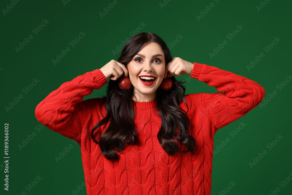 Happy woman trying Christmas balls as earrings on green background Happy woman trying Christmas balls as earrings on green background