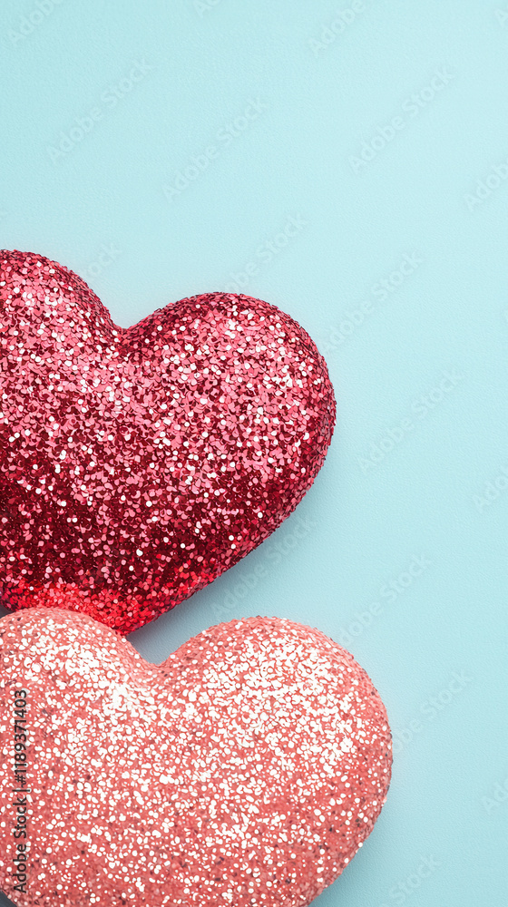 Fototapeta premium Glittery red and coral heart shapes on pastel blue background, evoking love and joy