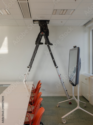 An electrician at work in a ceiling of a conference room in an office.