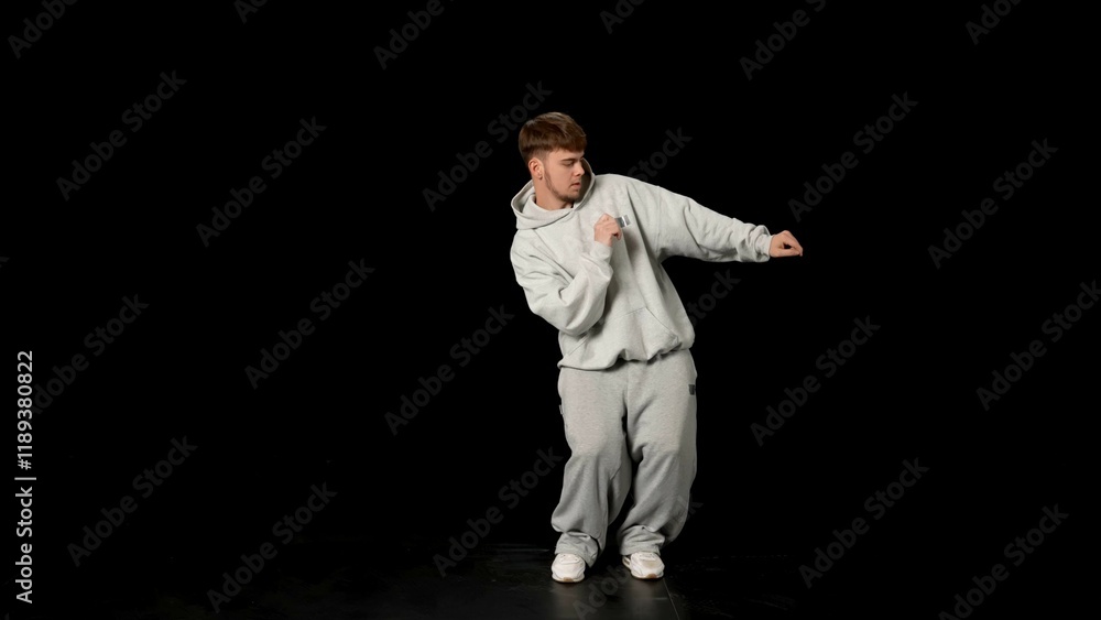 Young man in light gray clothes dancing hip-hop on black background Young man in light gray clothes dancing hip-hop on black background