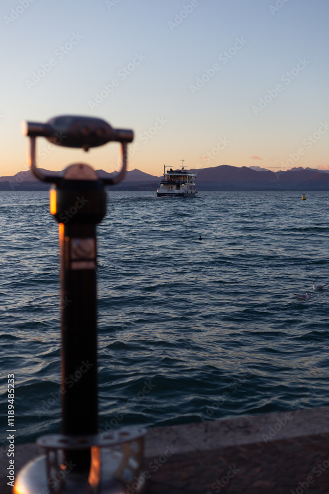 Sunset view of a boat on calm waters, captured through an out-of-focus telescope, with mountains fading into the horizon.