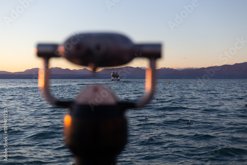Obraz na płótnie A boat approaches under a warm sunset, framed artistically by a blurred telescope and serene mountain scenery. w salonie