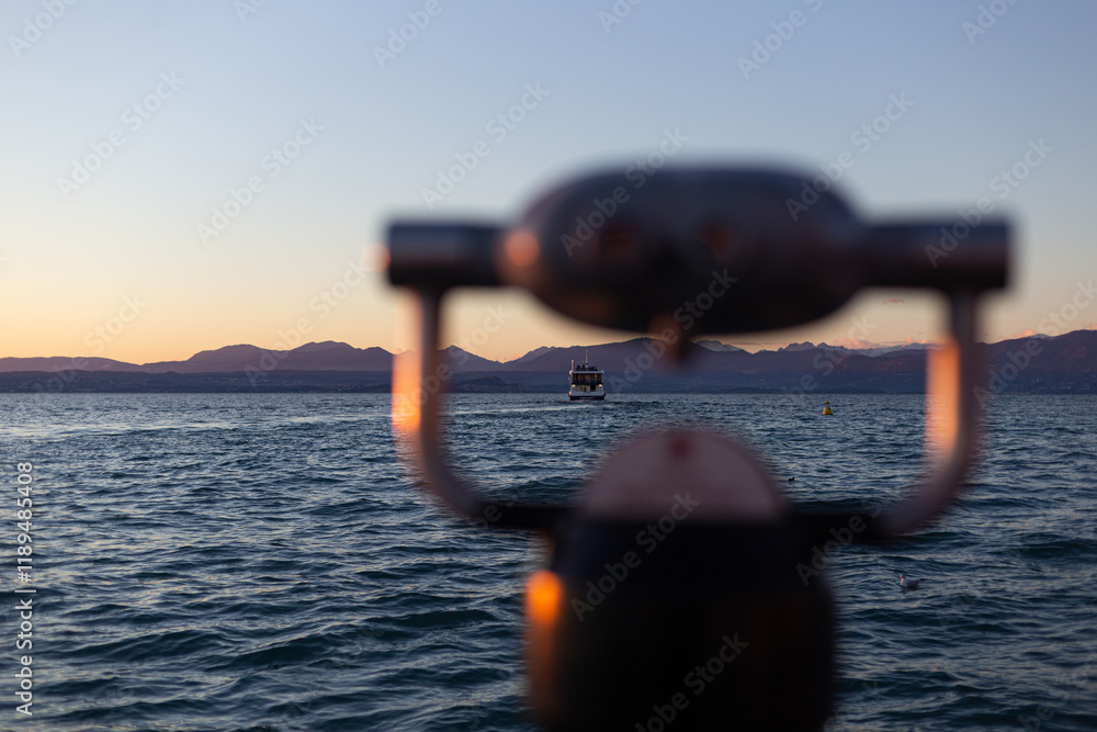 A scenic sunset featuring a distant boat, soft-focus telescope, and peaceful waters against a mountainous backdrop.