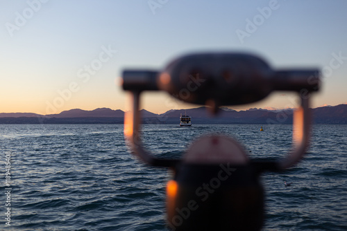 Obraz na płótnie A scenic sunset featuring a distant boat, soft-focus telescope, and peaceful waters against a mountainous backdrop. w salonie