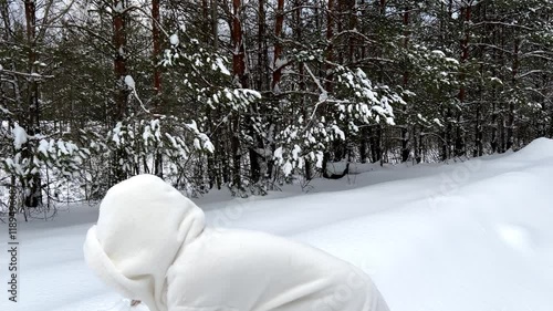 Girl in white winter coat in snowdrift having fun throwing snow on frosty day. Countryside on background. Snowy winter forest. High quality 4k footage photo