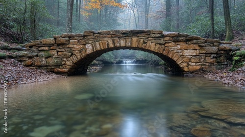 Stone bridge over calm water surrounded by autumn trees in a misty forest