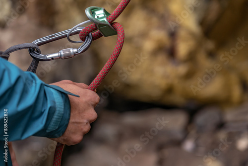 Close up of young man climber belaying leader during rock climbing outdoors, using rope, grigri, carabines and gloves. Concept of teamwork, trust, extreme sport and outdoor activity photo