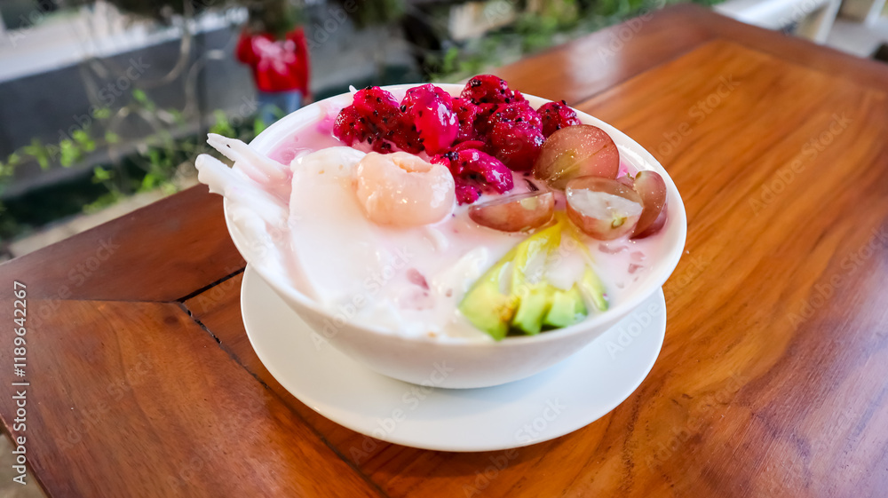 A bowl of colorful fruit dessert, including dragon fruit, grapes, avocado, and coconut slices, served with milk A bowl of colorful fruit dessert, including dragon fruit, grapes, avocado, and coconut slices, served with milk