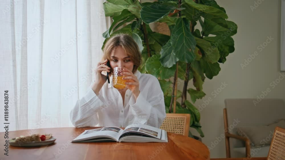 Casual woman calling smartphone drinking juice at home table with book closeup Casual woman calling smartphone drinking juice at home table with book closeup