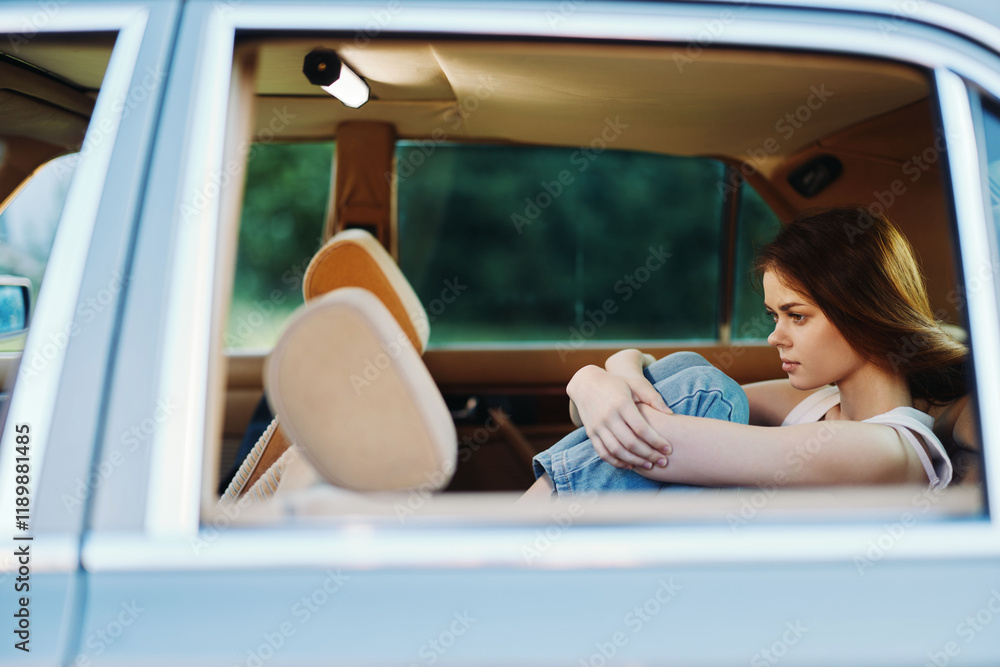 Naklejka premium Sad young woman in casual outfit sitting in the backseat of a car, expressing deep emotions and reflection amidst a blurred green background.