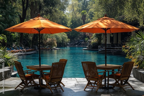 Wooden Table and Chairs by Pool in Front of Outdoor Resort Hotel, with Orange Umbrellas and Natural Sunlight, Symmetrical Composition. photo