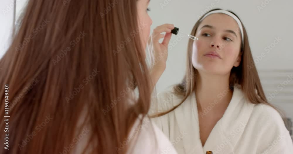Using dropper bottle, woman applying skincare serum in bathroom mirror reflection, at home Using dropper bottle, woman applying skincare serum in bathroom mirror reflection, at home