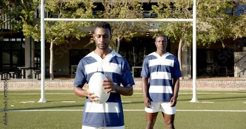 Holding rugby ball, two african american men in sports uniforms standing on field, copy space