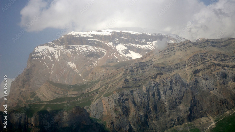 Fototapeta premium Giant ridge with snow under cloudy sky. Amazing mountain range in overcast weather. Unusual foggy rocks. Wonderful landscape of majestic nature of highlands. Caucasus Mountains, Shahdag