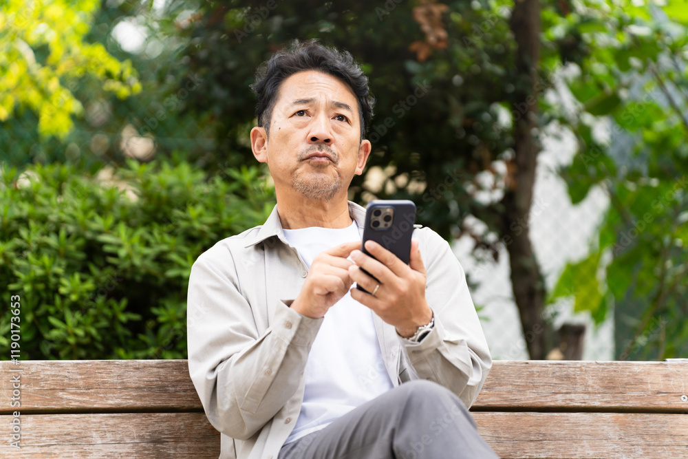 ベンチに座りならスマートフォンを操作するミドル男性 ベンチに座りならスマートフォンを操作するミドル男性