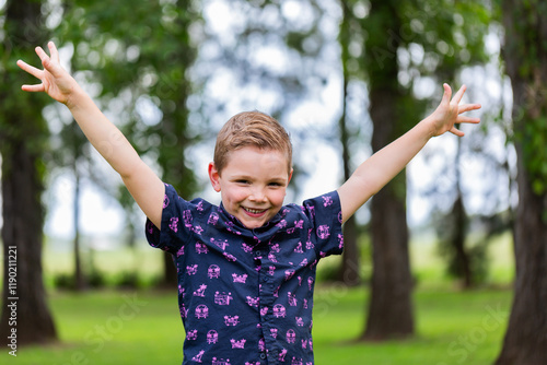 Portrait of kindergarten aged boy outdoors smiling with arms wide in celebration of success photo