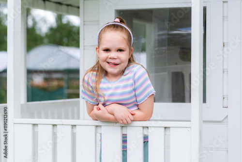 Little girl standing in play cubby house on farm smiling at camera