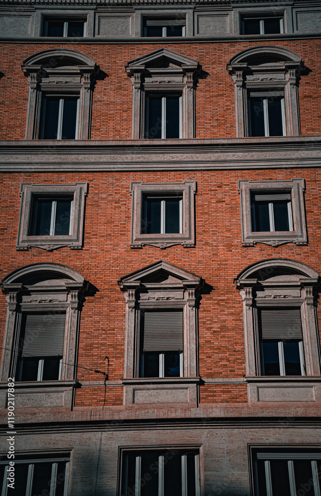 Obraz premium A beautiful red brick building with grey stone window frames, showcasing a perfect blend of classic architecture and rustic charm. A timeless piece of craftsmanship in the heart of the city.