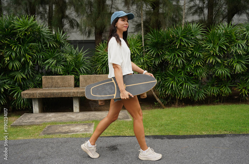 A woman is walking at the city park while carrying a skateboard in her hands photo