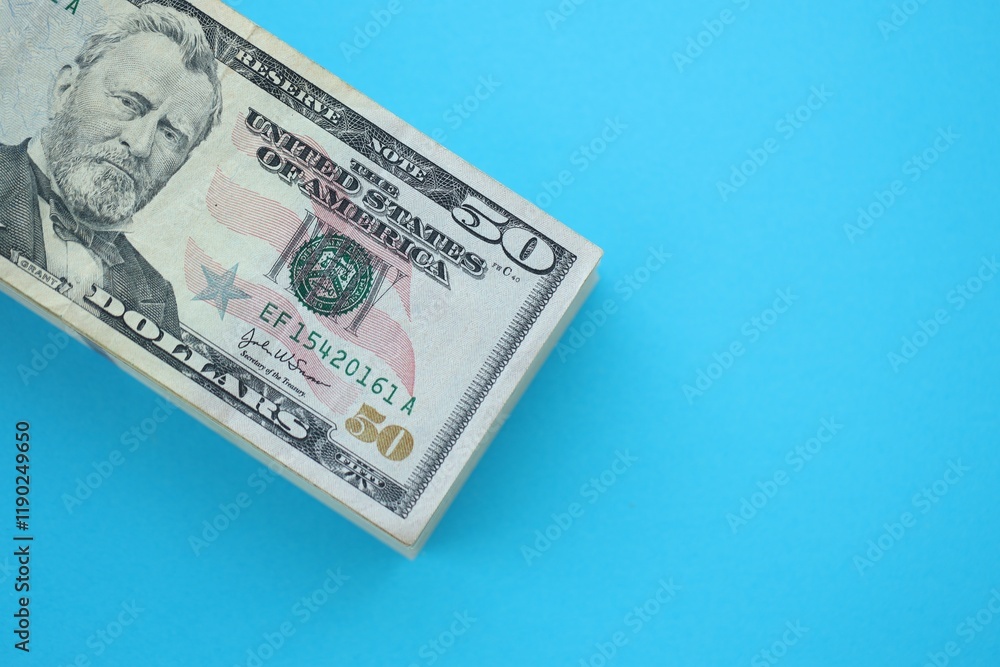 Big amount of fifty dollar bills in thick stack lies on bright blue color paper background Big amount of fifty dollar bills in thick stack lies on bright blue color paper background