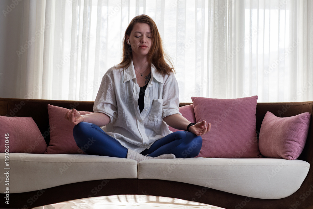 Young woman meditating on couch at home Young woman meditating on couch at home