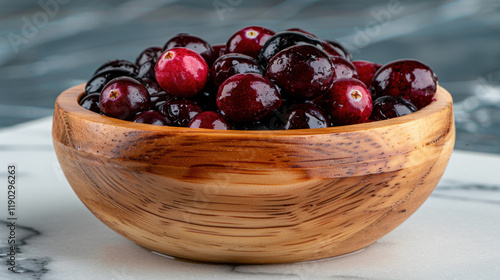 A rustic wooden bowl filled with glossy, fresh cranberries placed on a marble surface, highlighting their natural texture and vibrant color.
 photo