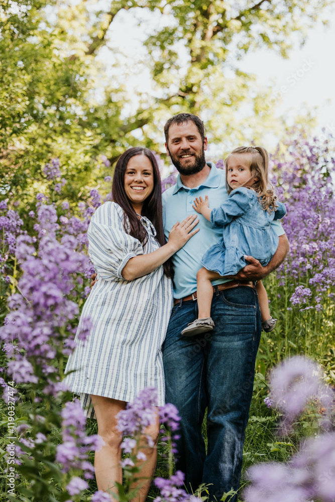 Family stands in a field of purple wildflowers while looking at camera Family stands in a field of purple wildflowers while looking at camera