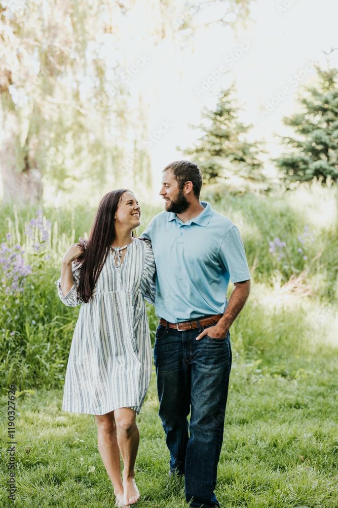 Man and wife walk with arms wrapped around each other through park Man and wife walk with arms wrapped around each other through park