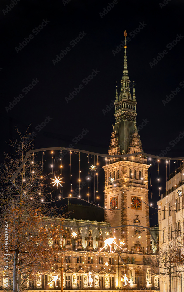 Blick auf den Turm des beleuchteten Rathauses in Hamburg während der Weihnachtszeit, Weihnachtslichter im Vordergrund, vertikal Blick auf den Turm des beleuchteten Rathauses in Hamburg während der Weihnachtszeit, Weihnachtslichter im Vordergrund, vertikal