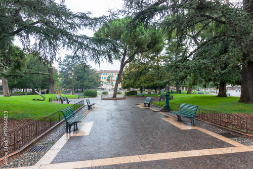 A tranquil scene in the park located on Piazza Bra, Verona, Italy, featuring paved walkways, green lawns, various trees, and benches for visitors photo