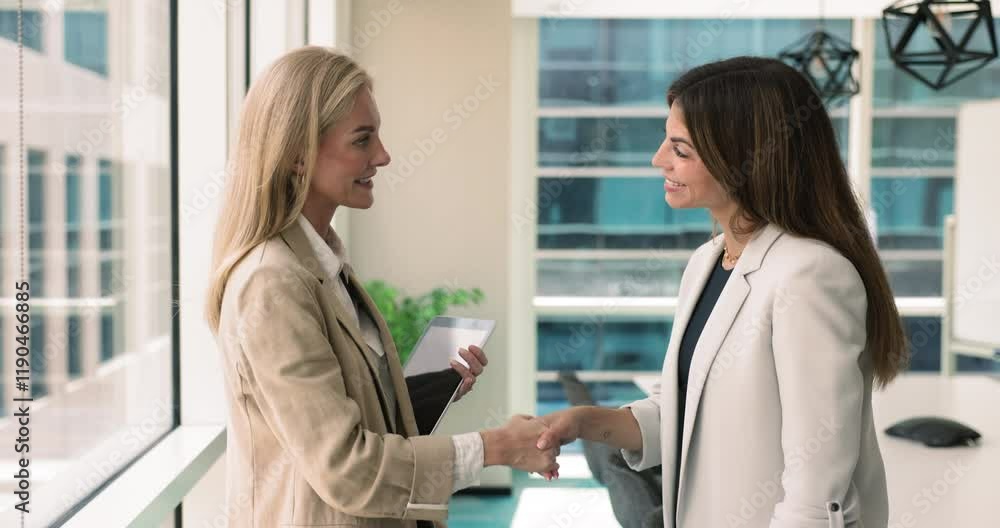 Happy diverse female business partners talking and shaking hands in office, smiling, finishing meeting. Young businesswoman giving gratitude handshake to mentor, coach, boss woman Happy diverse female business partners talking and shaking hands in office, smiling, finishing meeting. Young businesswoman giving gratitude handshake to mentor, coach, boss woman