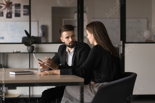 Two young Caucasian teammates involved in dialogue in meeting room, to sharing ideas, creative thoughts and business vision, gathered for decision-making, take part in productive teamwork in office