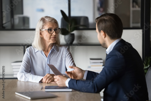 Wallpaper Mural Two colleagues discussing project marketing strategy in office. Professional insurance agent holds paper explains policy terms and conditions with female client seated at table. Negotiations, meeting Torontodigital.ca