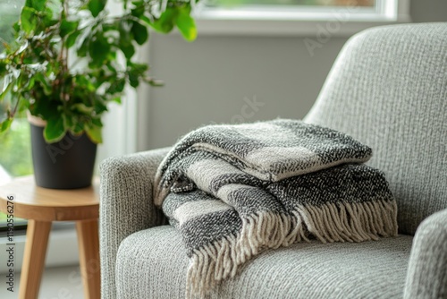 A neatly folded boucle plaid sits on a chair beside a plant photo