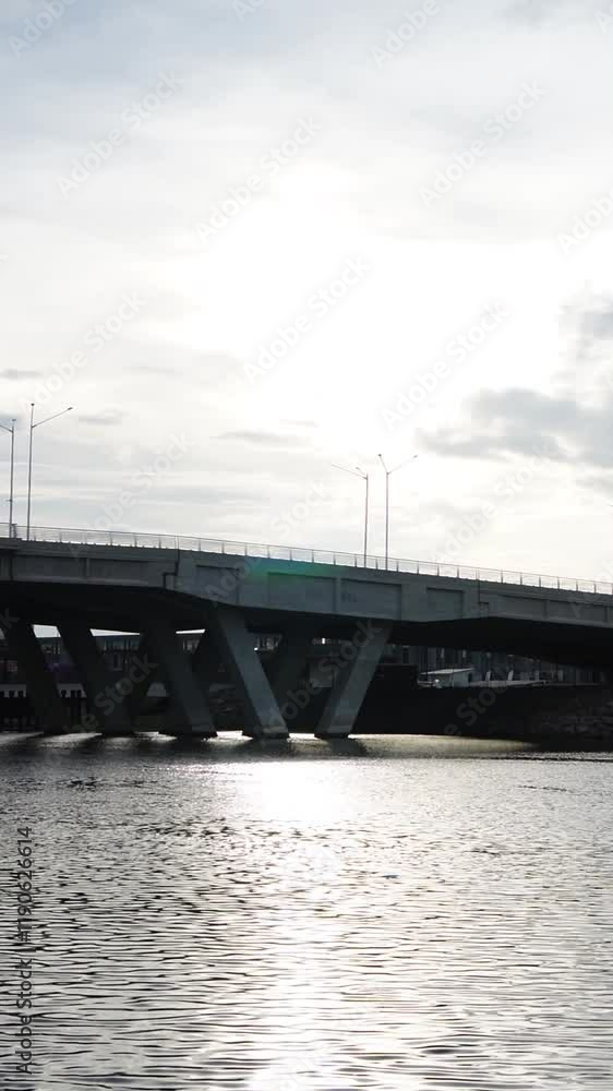 Slow Motion of Car Passing Modern Bridge Over Calm River with Water Reflecting Under Daylight Slow Motion of Car Passing Modern Bridge Over Calm River with Water Reflecting Under Daylight