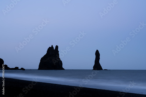 Stunning view of Reynisdrangar basalt sea cliffs during a cloudy day. Reynisfjara is a world-famous black-sand beach found on the South Coast of Iceland. photo