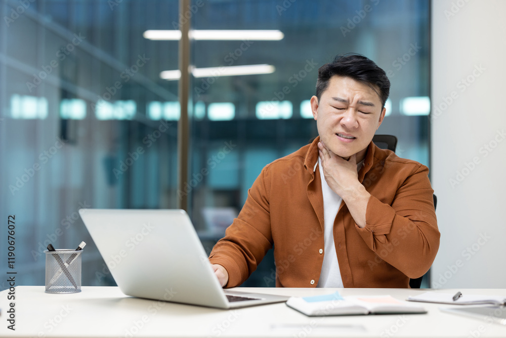 Asian sick man at workplace has sore throat, severe sore throat pain. Man with cold working inside office at workplace. Asian sick man at workplace has sore throat, severe sore throat pain. Man with cold working inside office at workplace.